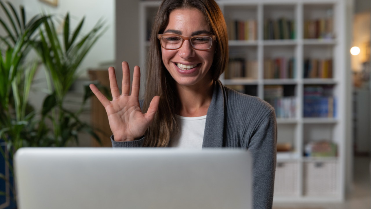 Woman with glasses waving and smile to someone on laptop screen 